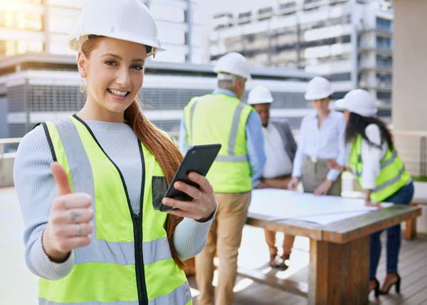 Cropped portrait of an attractive young female construction worker using a cellphone while standing outside with her team in the background
